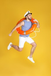 Photo of Emotional sailor with ring buoy jumping on yellow background