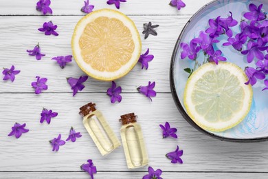 Bowl with water, lemon, purple flowers and bottles of essential oils on white wooden table, flat lay. Spa composition