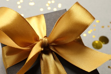 Photo of Beautiful black gift box with golden bow on grey background, closeup