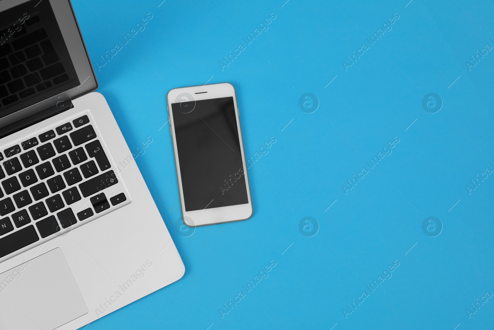 Photo of Modern laptop and smartphone on blue background, top view. Space for text