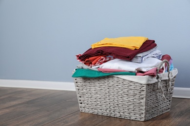 Photo of Wicker laundry basket with clean clothes on floor near color wall. Space for text
