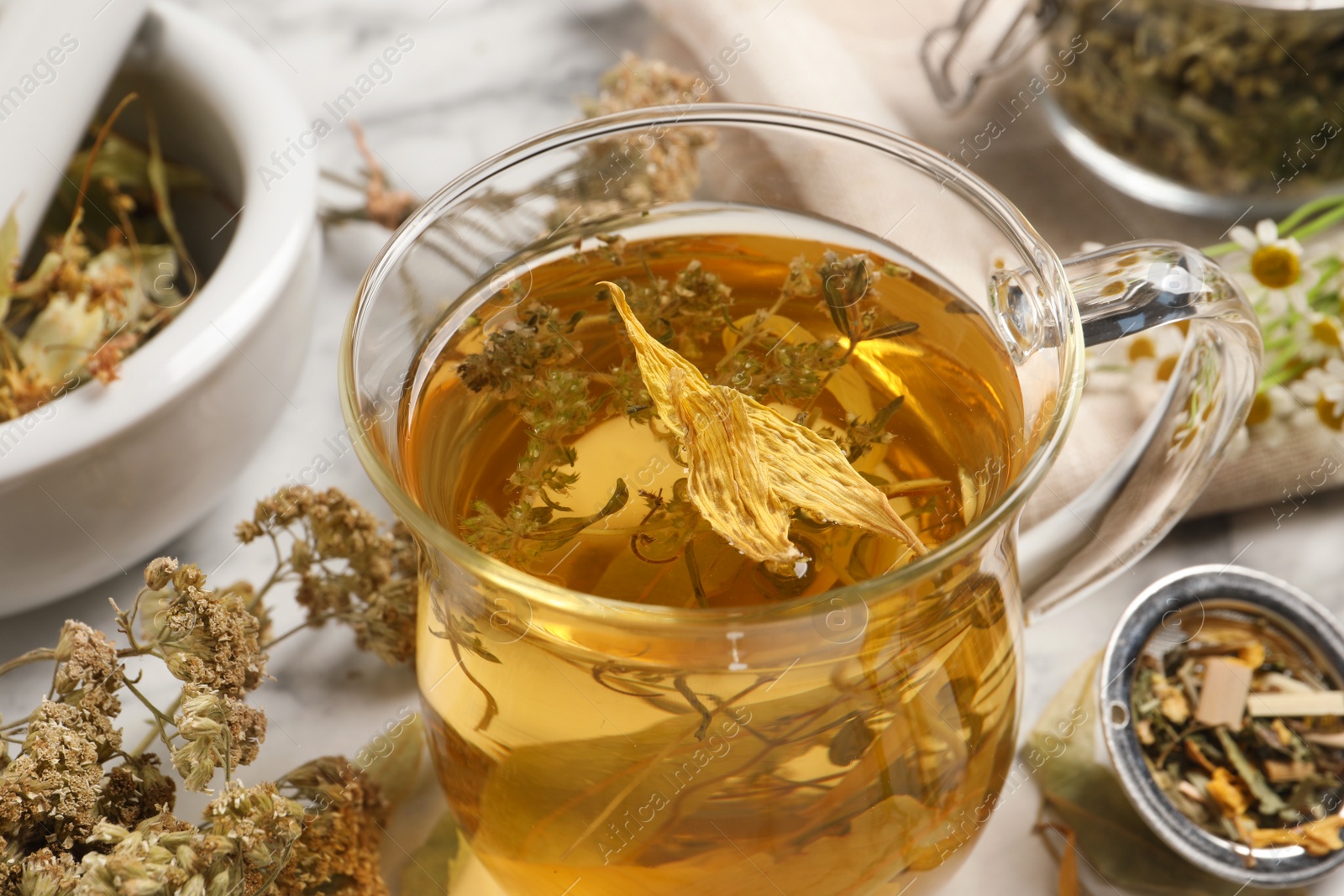 Photo of Freshly brewed tea and dried herbs on white marble table, closeup