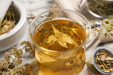 Photo of Freshly brewed tea and dried herbs on white marble table, closeup