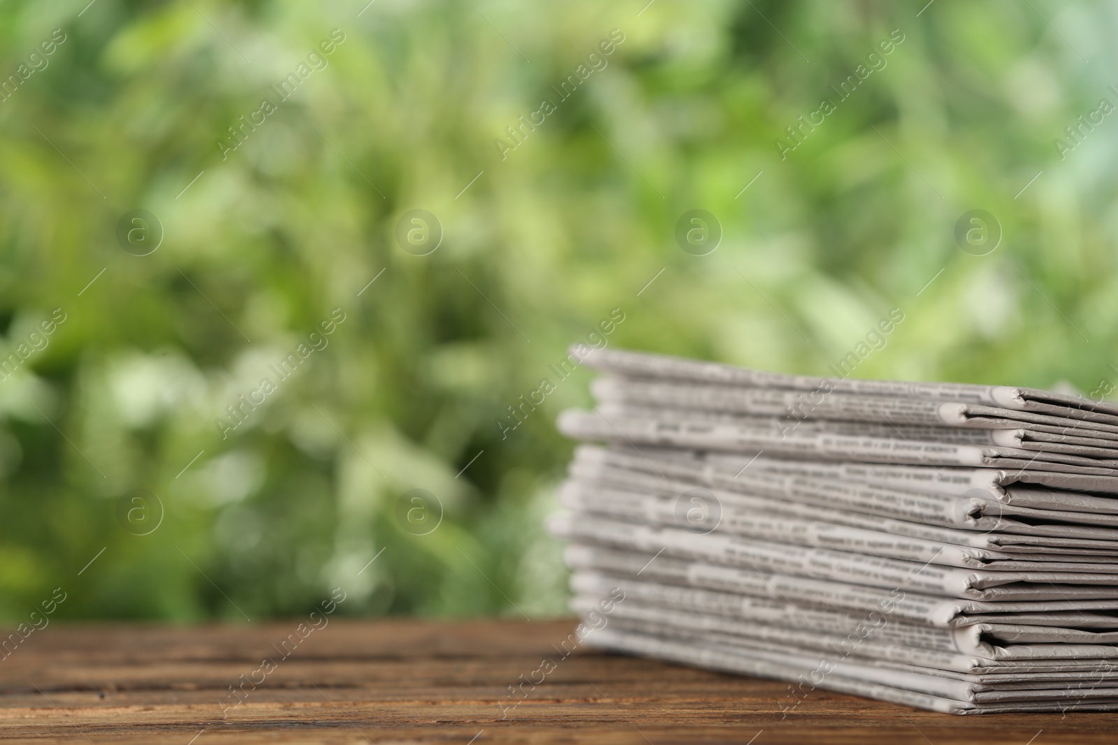 Photo of Stack of newspapers on wooden table against blurred green background, space for text. Journalist's work