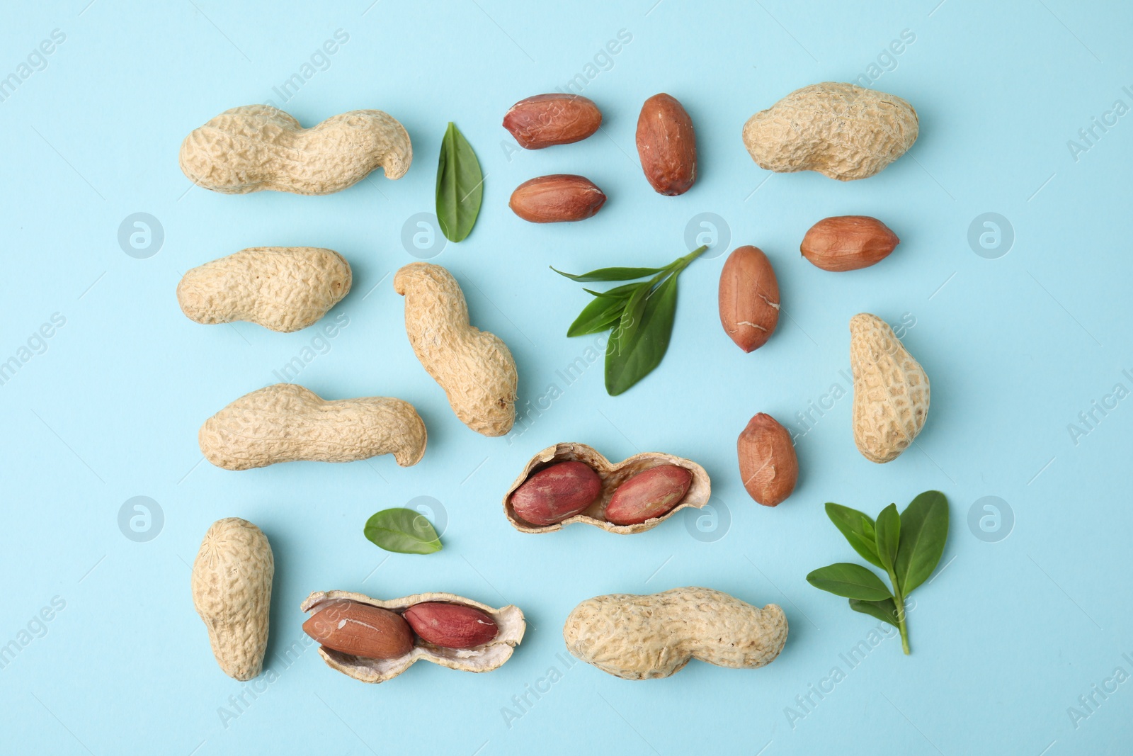 Photo of Fresh peanuts and leaves on light blue table, flat lay