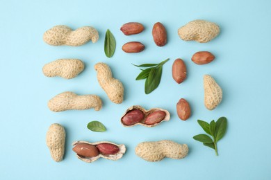 Fresh peanuts and leaves on light blue table, flat lay