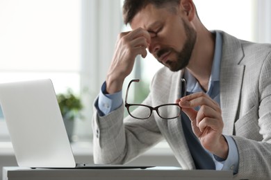 Photo of Man suffering from eyestrain in office, focus on hand with glasses