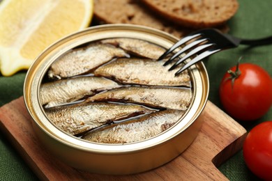 Photo of Canned sprats, fork and tomatoes on table, closeup