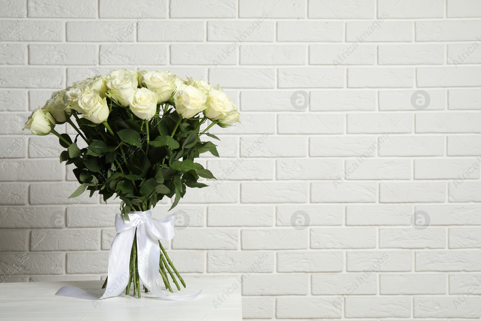 Photo of Luxury bouquet of fresh roses on table near white brick wall, space for text