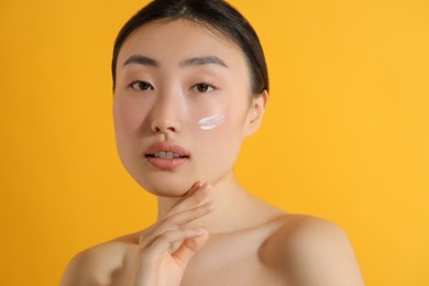 Photo of Beautiful young woman with sun protection cream on her face against orange background