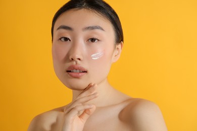 Beautiful young woman with sun protection cream on her face against orange background