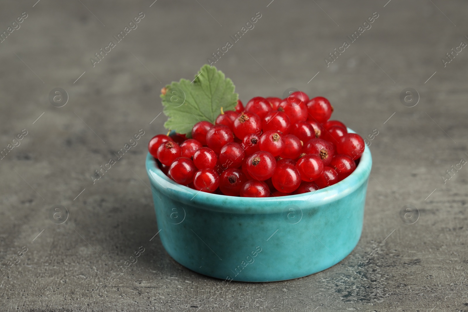 Photo of Ripe red currants and leaf in bowl on dark textured table, closeup