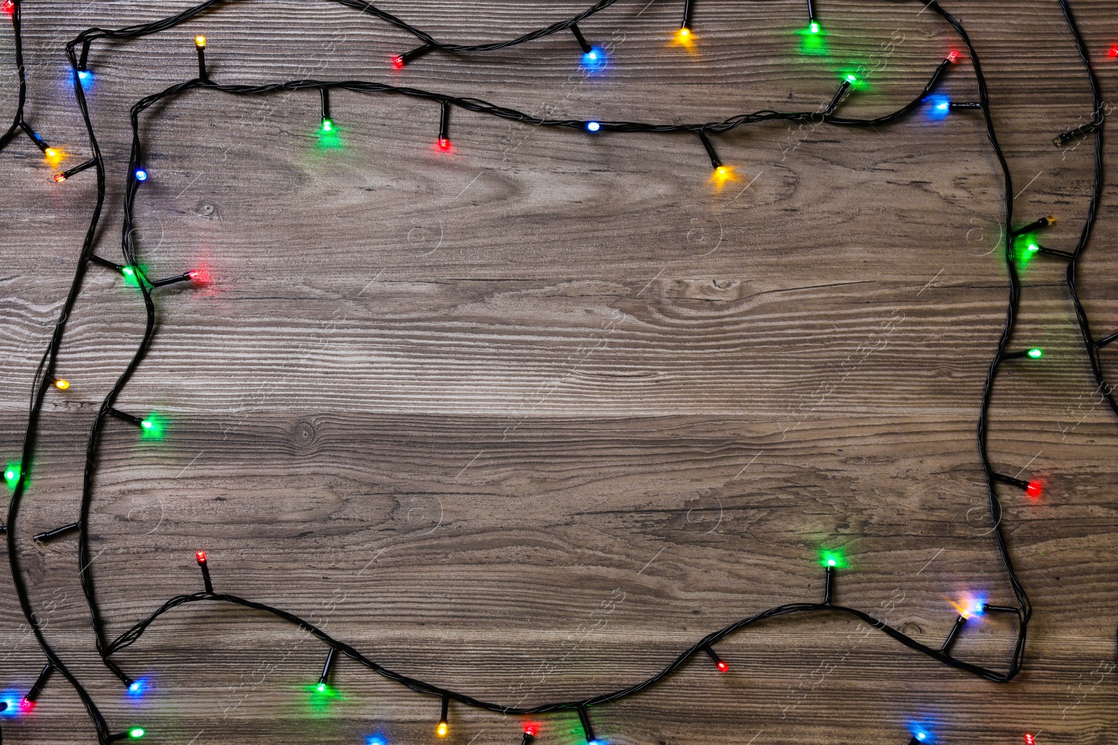 Photo of Frame of Christmas lights on wooden table, top view. Space for text