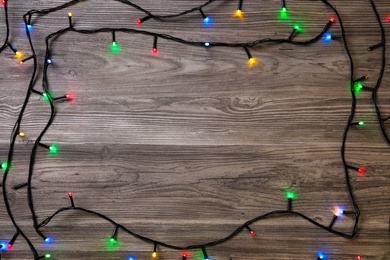 Photo of Frame of Christmas lights on wooden table, top view. Space for text