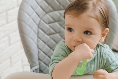 Cute little baby nibbling teether in high chair indoors, closeup. Space for text