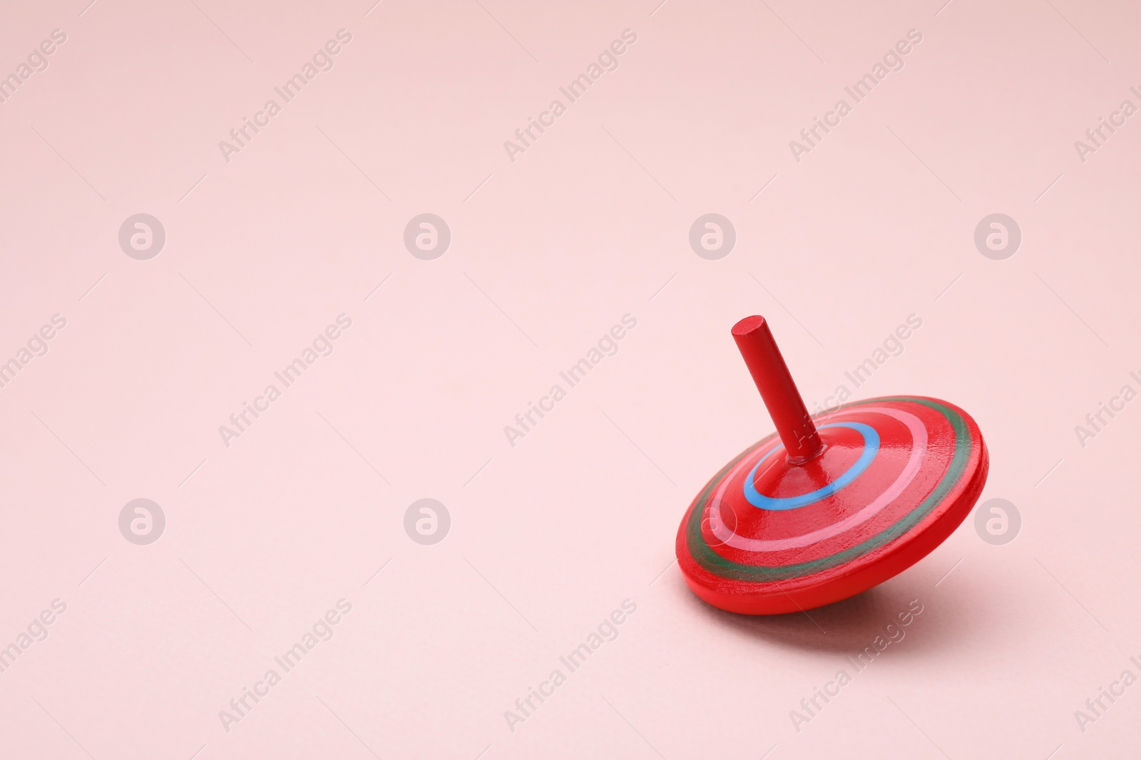 Photo of One bright spinning top on beige background, space for text. Toy whirligig
