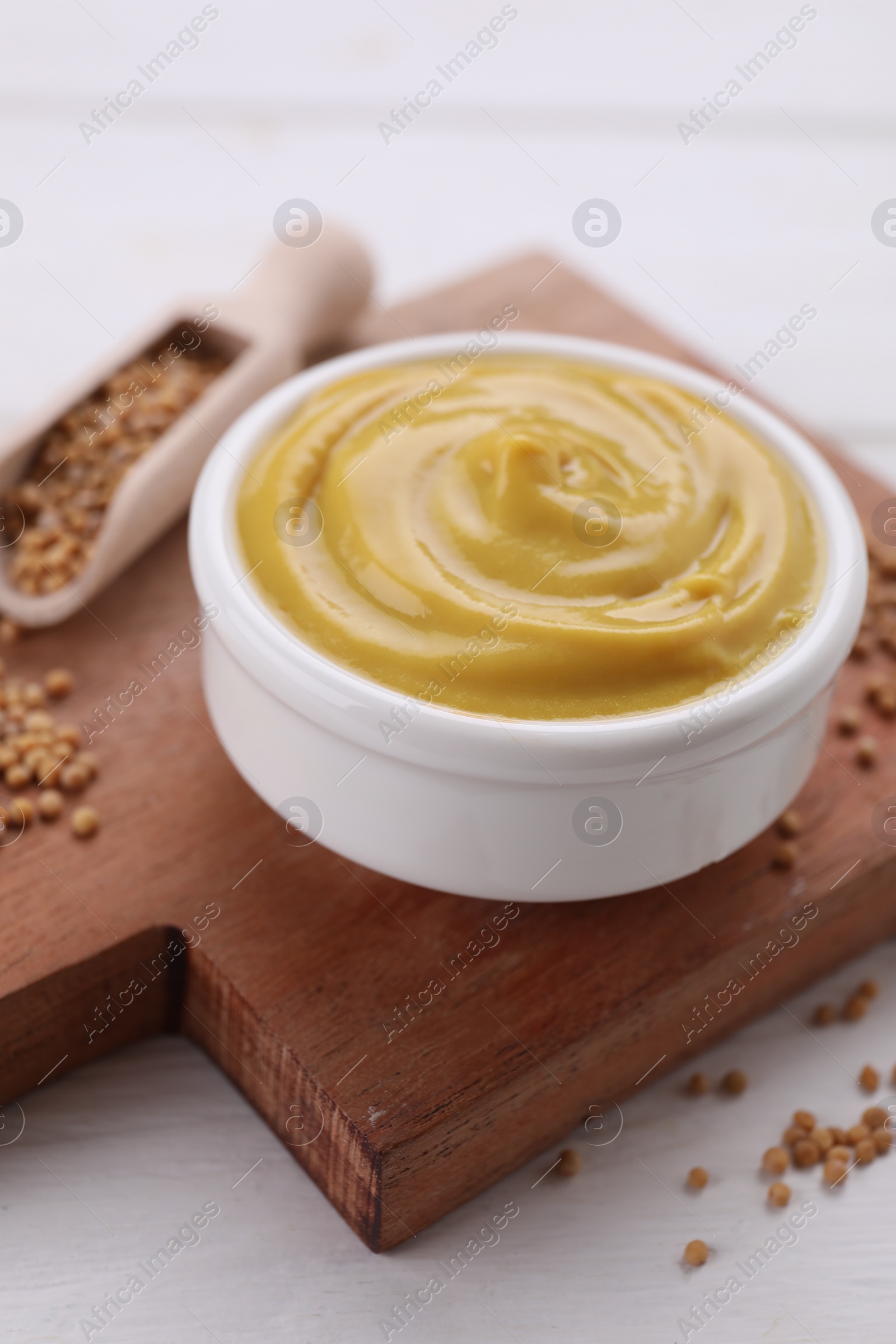 Photo of Bowl with delicious mustard and seeds on white wooden table