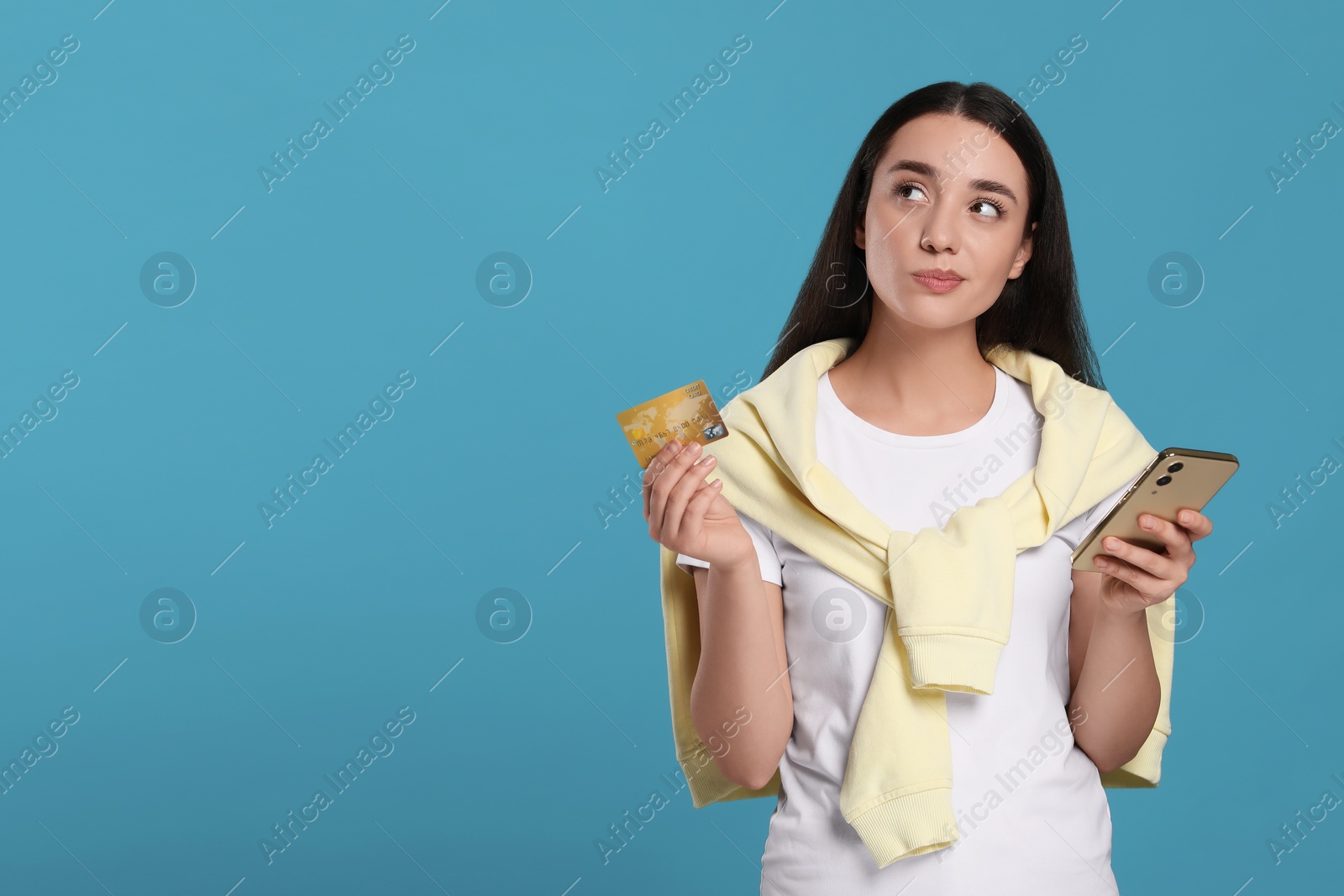 Photo of Confused woman with credit card and smartphone on light blue background, space for text. Debt problem