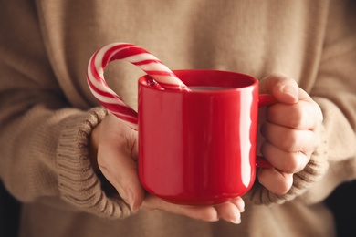 Photo of Woman holding cup of tasty cocoa with Christmas candy cane, closeup