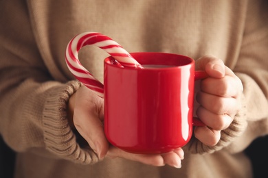 Woman holding cup of tasty cocoa with Christmas candy cane, closeup