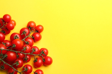 Branches with fresh cherry tomatoes on yellow background, flat lay. Space for text