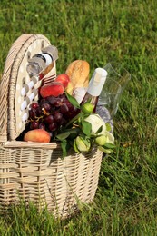 Photo of Picnic basket with tasty food, flowers and cider on grass