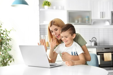 Mother and her son using video chat on laptop at table in kitchen