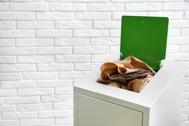 Photo of Trash bin with paper and cardboard near brick wall, space for text. Recycling concept