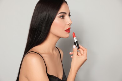 Young woman with beautiful makeup holding red lipstick on light gray background