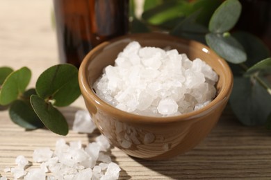 Spa composition with sea salt and eucalyptus leaves on wooden table, closeup