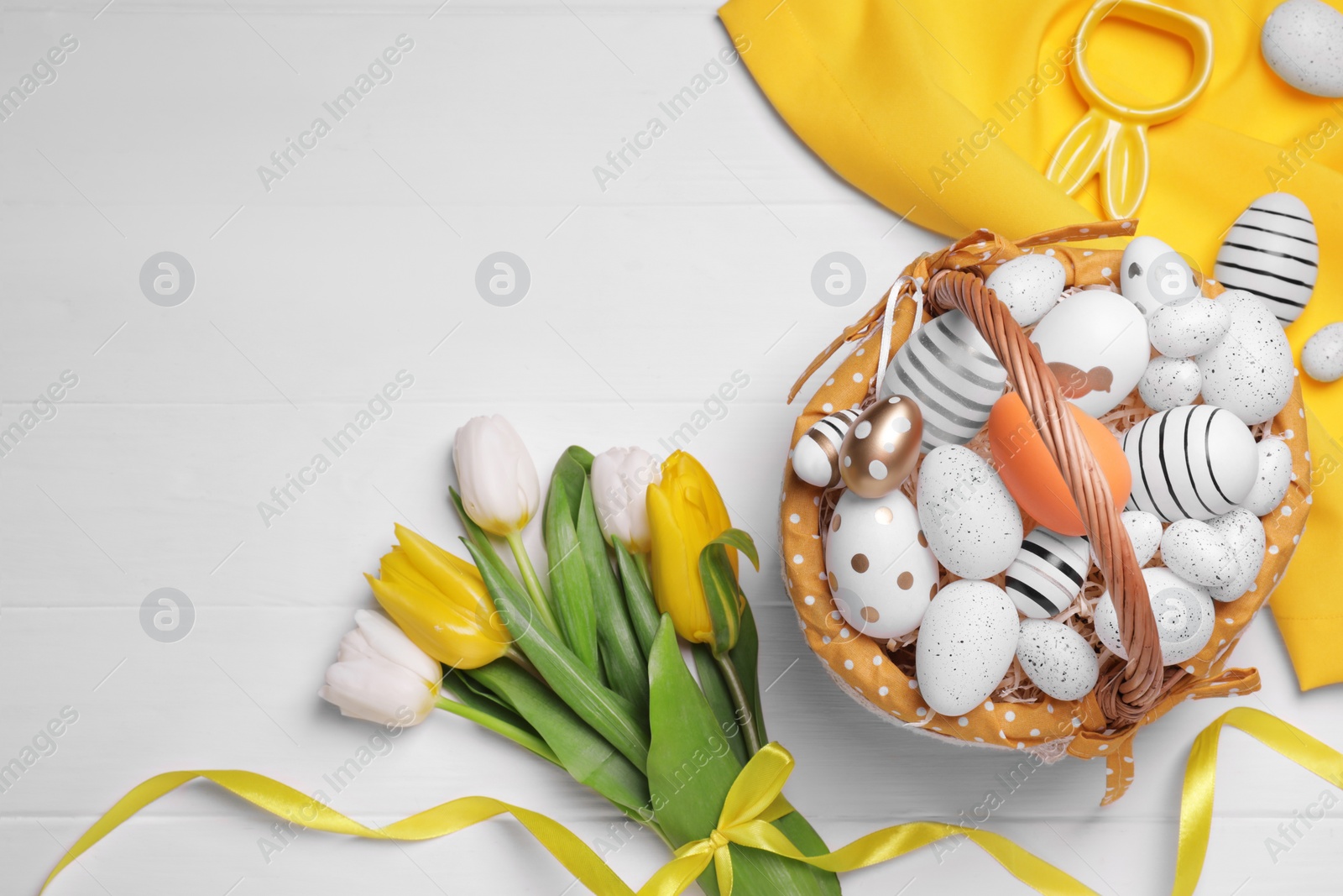 Photo of Flat lay composition with Easter eggs in basket and tulips on white wooden table. Space for text