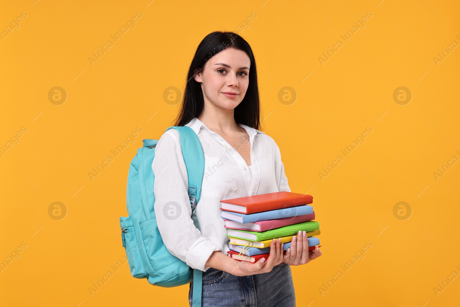 Photo of Student with stack of books on yellow background