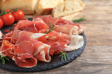 Photo of Pile of tasty prosciutto on wooden table, closeup