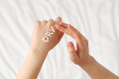 Photo of Young woman with word Dry made of cream on her hand on bed, closeup