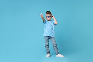 Photo of Happy little boy dancing on light blue background. Space for text