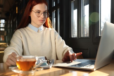 Photo of Young female student with laptop studying at table in cafe