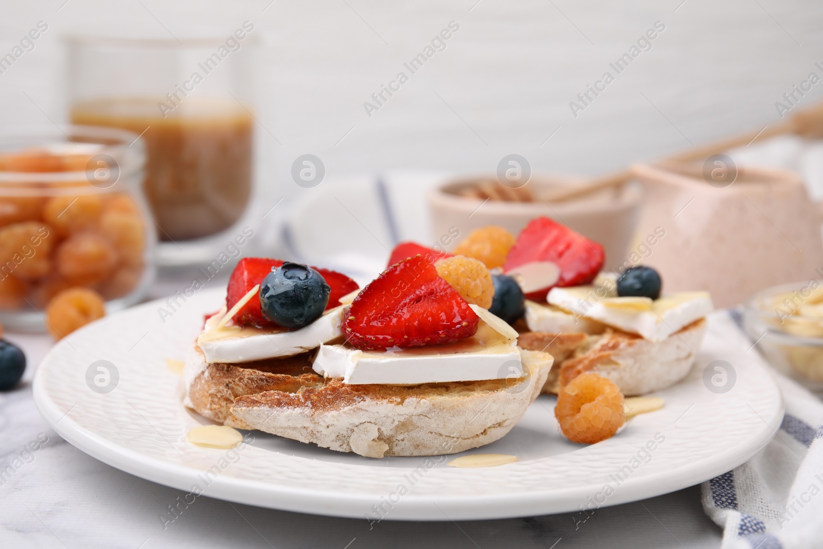 Photo of Tasty sandwiches with brie cheese, fresh berries and almond flakes on white marble table, closeup