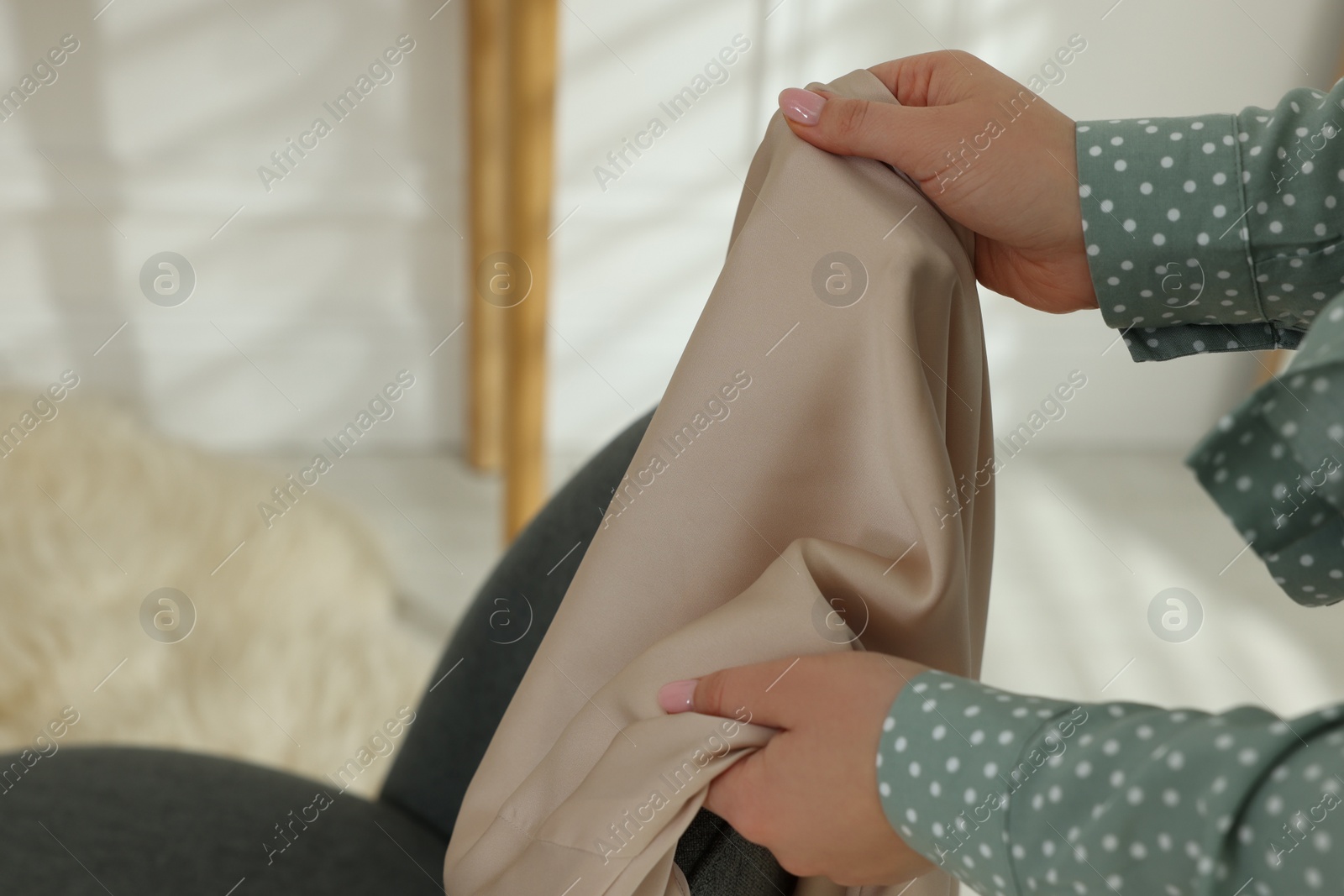 Photo of Woman touching dress made of smooth beige fabric indoors, closeup