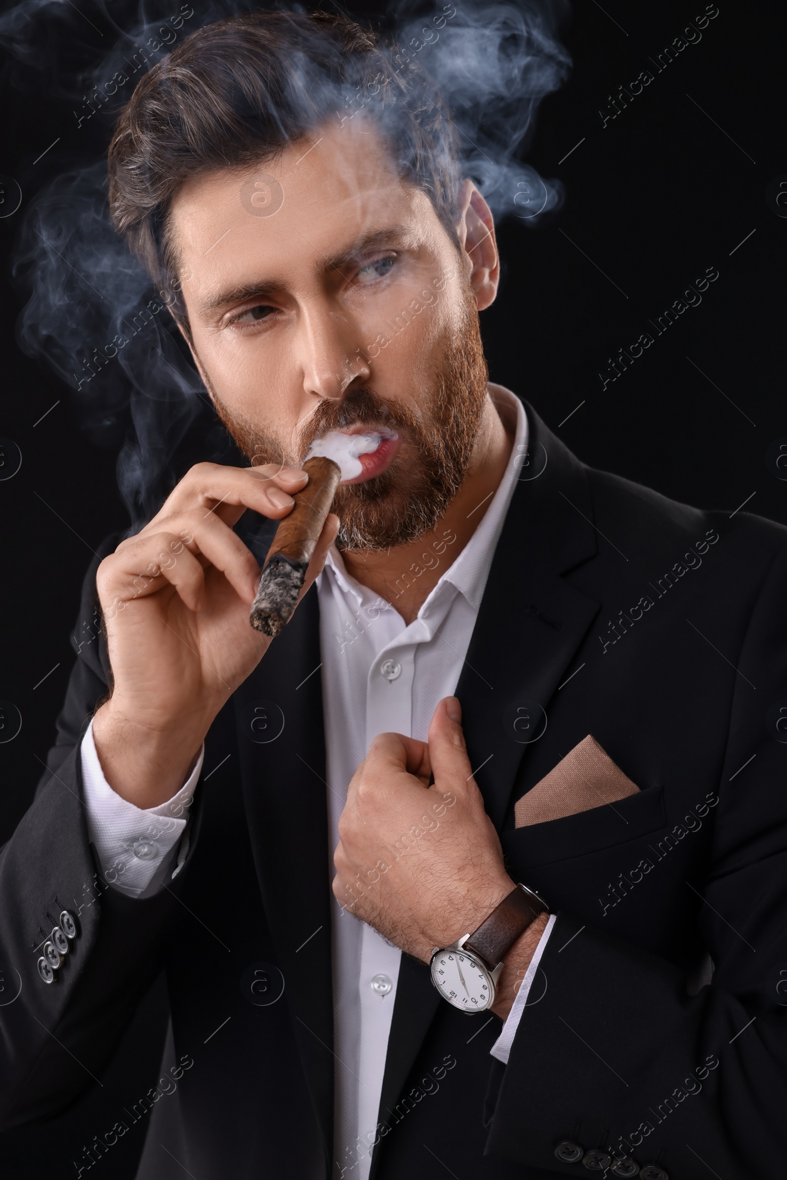 Photo of Handsome man in elegant suit smoking cigar on black background