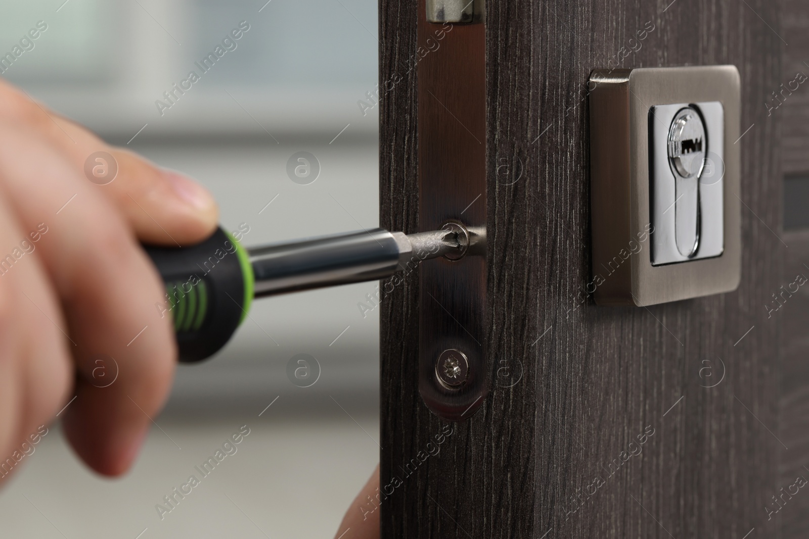 Photo of Handyman with screwdriver repairing door lock indoors, closeup