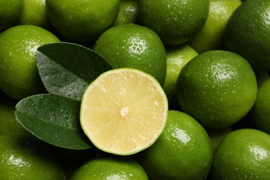 Fresh limes and leaves with water drops as background, top view