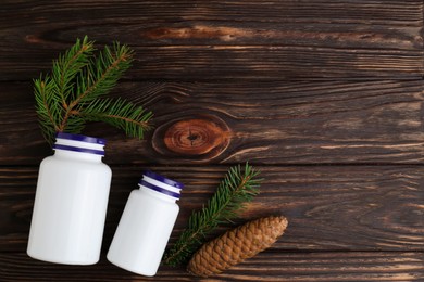 Photo of White medical bottles, spruce twigs and cone on wooden table, flat lay. Space for text