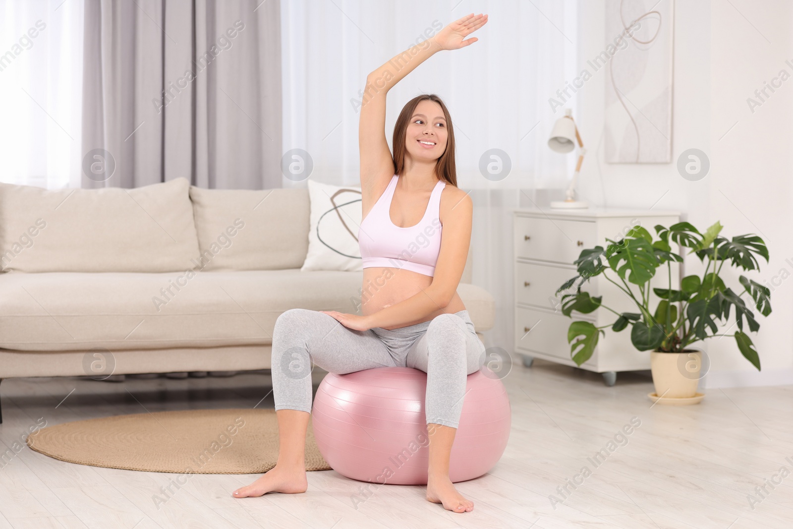 Photo of Pregnant woman doing exercises on fitness ball in room. Home yoga