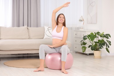 Photo of Pregnant woman doing exercises on fitness ball in room. Home yoga