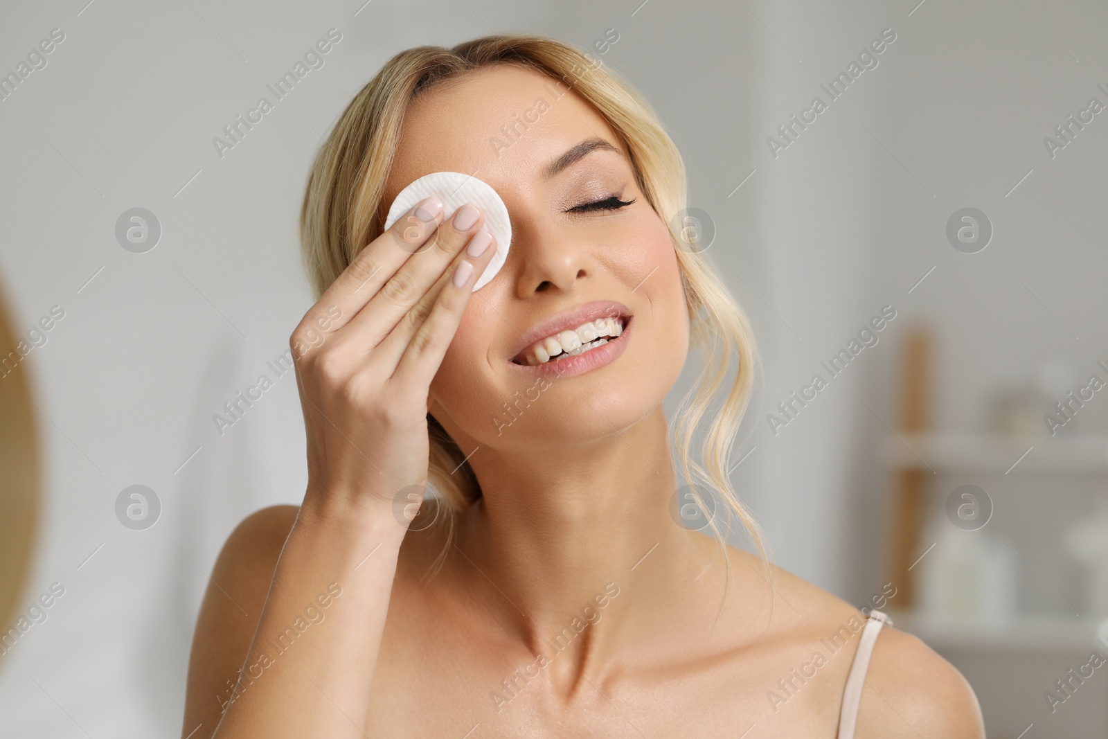 Photo of Smiling woman removing makeup with cotton pad indoors