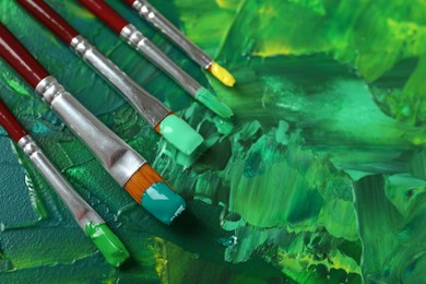 Photo of Set of different brushes on abstract colorful paint, closeup