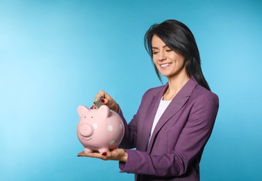 Beautiful businesswoman putting money into piggy bank on color background. Space for text