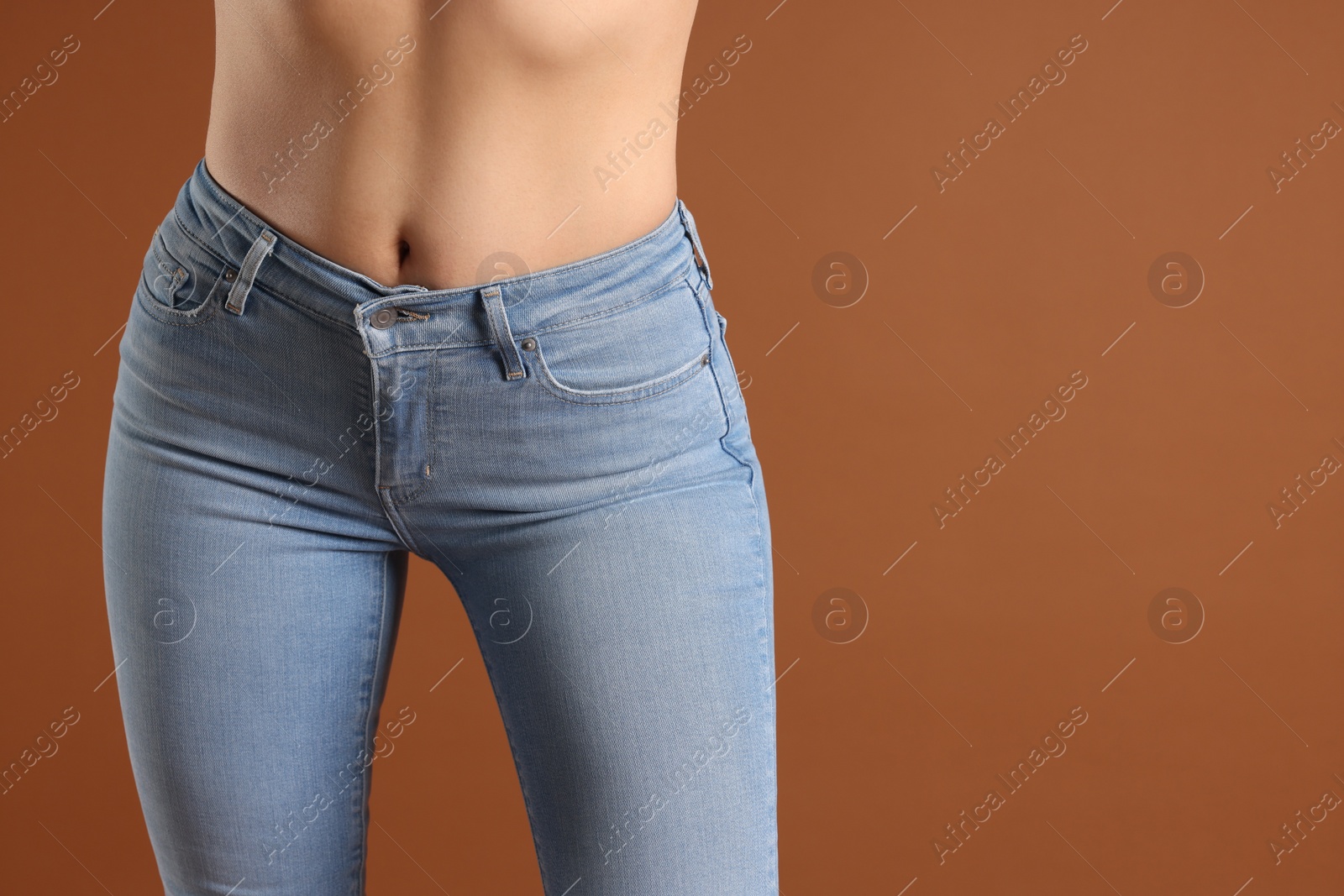 Photo of Woman wearing stylish light blue jeans on brown background, closeup. Space for text