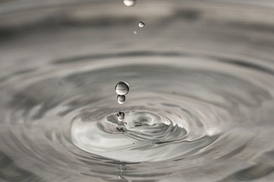 Photo of Drops falling into clear water on grey background, closeup