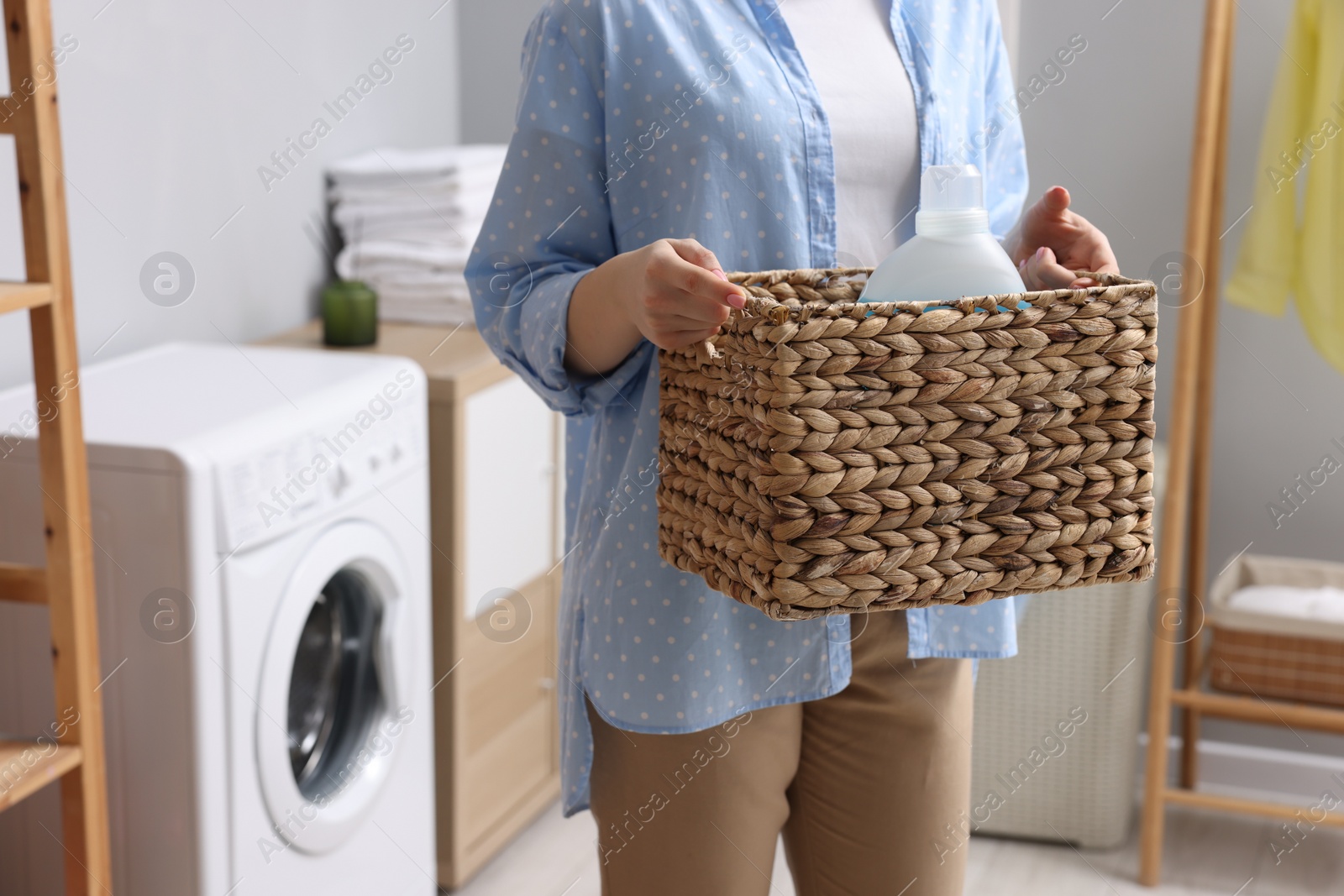 Photo of Woman holding wicker basket with detergent in laundry room, closeup